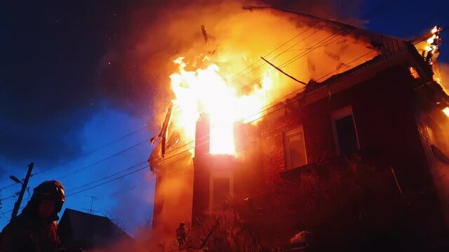 The roof of the house is on fire. The residential building burn, village. Firefighters put out a fire from the crane from above. Smoke and sparks.
