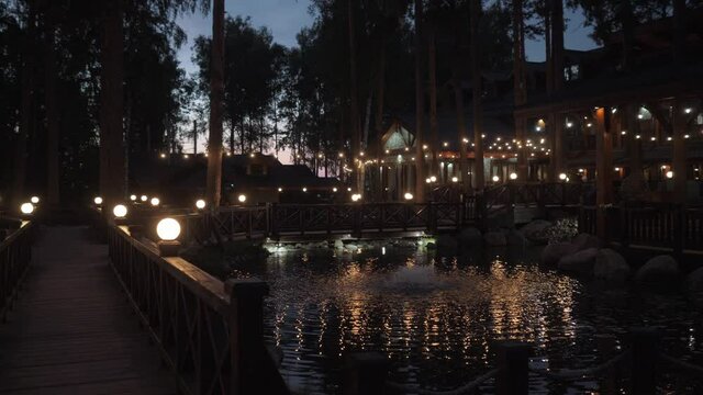 Beautiful territory of a country restaurant with bridges in reservoirs and burning lanterns at night. High quality FullHD footage