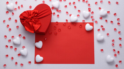 Happy valentines day arrangement. Red heart-shaped gift box with red glass decorative beads and white heart shaped decoration on a white-red background. Flat lay. Copy text.