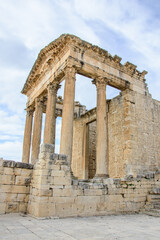 Fototapeta premium Portico of the ruined temple of Jupiter in the ancient roman city of Dougga in Tunisia, Africa. Blue sky with clouds, old yellow, grey and brown stone walls and columns