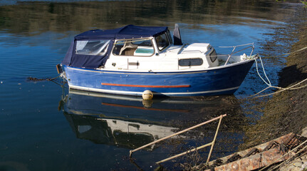 Small boats moored in a Cornish harbour, bright blue water with reflections & shadows