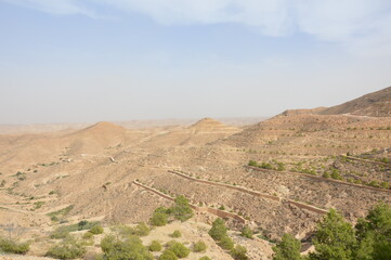 Deserted hills near Matmata in Tunisia, Africa. Blue sky with clouds, yellow sandy hills, rare green trees