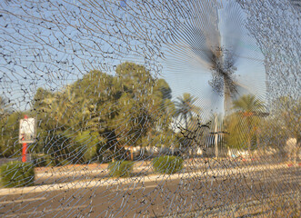 Defocused view of a palm trees and road  in Tunisia, Africa, through a broken glass of the train window. Blue sky, grey asphalt, green leaves and radial cracks on the glass.