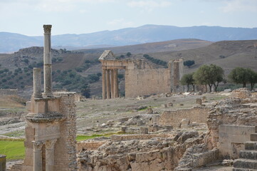 Ruins of the ancient Roman theatre and the temple of Jupiter in Dougga, Tunisia, Africa. Blue sky with clouds, old yellow, grey and brown stone walls and columns with capitels