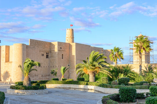 Ancient arabic ribat fortress walls, windows and tower in Monastir, Tunisia, Africa. blue sky, yellow stones, sunlight on the walls, red tunisian in the sky above the tower