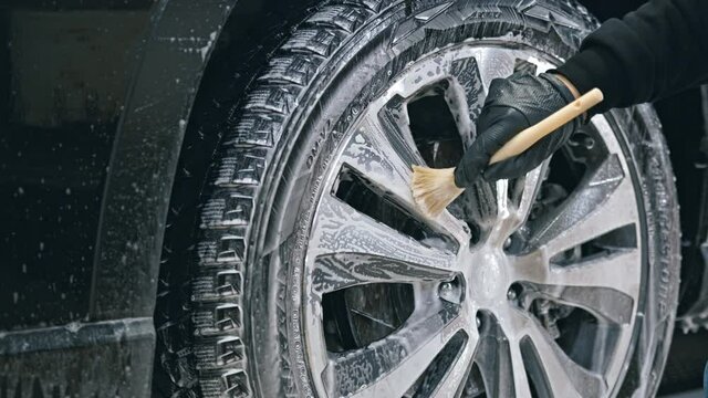 Close up of hand of worker man washes and scrubs car wheels with special brush. Carwash or Car Detailing process	