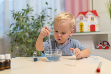 little boy child blonde play chemical experiments to sit at the table at home.