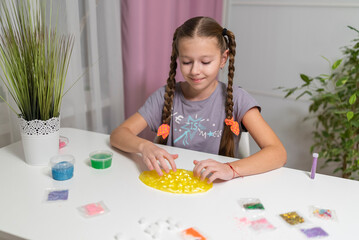 teen girl playing with green shiny slime at the table at home