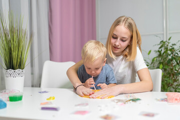 Naklejka premium sister and little brother play with yellow slime at table fun at home.