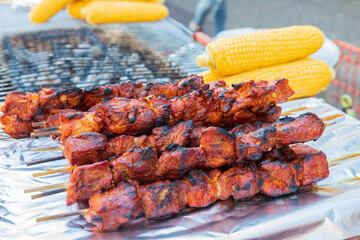 Meat kebabs and corn on the cob at a sidewalk food stand.