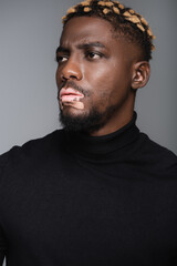 Fototapeta premium serious african american man with vitiligo and stylish hairstyle looking away isolated on grey.