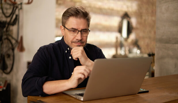 Casual man working with laptop computer in home office, happy, smiling. Mature age, middle age, mid adult man in 50s, white caucasian,