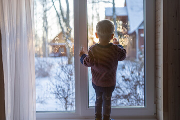 little boy stand near the window and look at the snowy street in winter, when it is very cold
