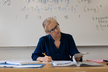 Portrait of high school math teacher sitting at desk working on assignments for students.