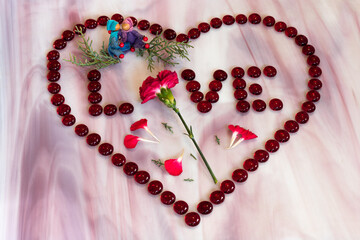 Obraz premium Red carnation inside a heart of red glass beads spelling LOVE with gender neutral elves hugging