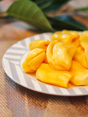 Jackfruit is fresh in a white plate, placed on a wooden table with jackfruit branches.