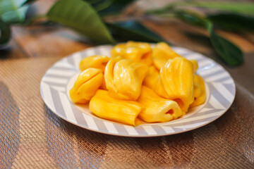 Jackfruit is fresh in a white plate, placed on a wooden table with jackfruit branches.
