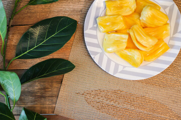 Jackfruit is fresh in a white plate, placed on a wooden table with jackfruit branches.