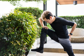 Happy Asian young sportsman doing a lower and upper body stretching before making an exercise in a park.