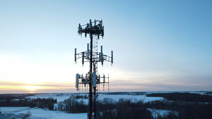 A radio tower stands silhouetted as the sun sets in winter background - Powered by Adobe