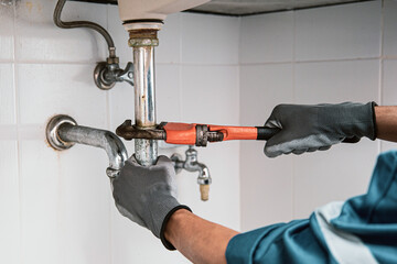 Technician plumber using a wrench to repair a water pipe under the sink. Concept of maintenance,...