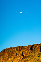 moon over a desert cliff during the day