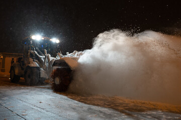 Tractor with rotary sweeper clearing city street at night after heavy snowfall. Clearing city by...