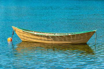 A close up of a single long yellow wooden dory with a red interior and green trim floating in blue...