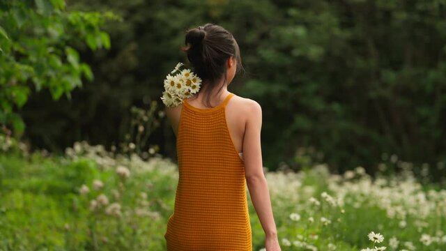 back view of young charming asian woman in yellow dress holding A bunch of flowers walking in the spring flower field