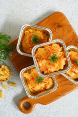 selective focus of  baked macaroni and cheese  in aluminium foil cup against white background 