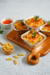 selective focus of  baked macaroni and cheese  in aluminium foil cup against white background 