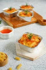 selective focus of  baked macaroni and cheese  in aluminium foil cup against white background 