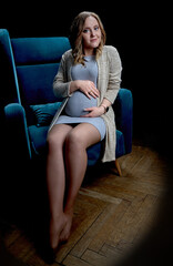 A pregnant woman is sitting on a blue chair and caressing her stomach. Mom Is Expecting A Baby. The concept of motherhood.