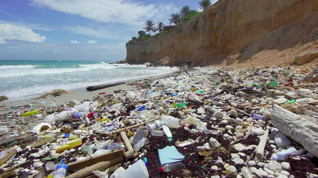 Tropical peninsula beach covered in plastic waste. Ocean waves wash plastic containers ashore and pollute the ecology and the environment.
