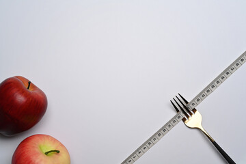 Fork with measuring tape and apples on white background. Loss weight and healthy diet concept.