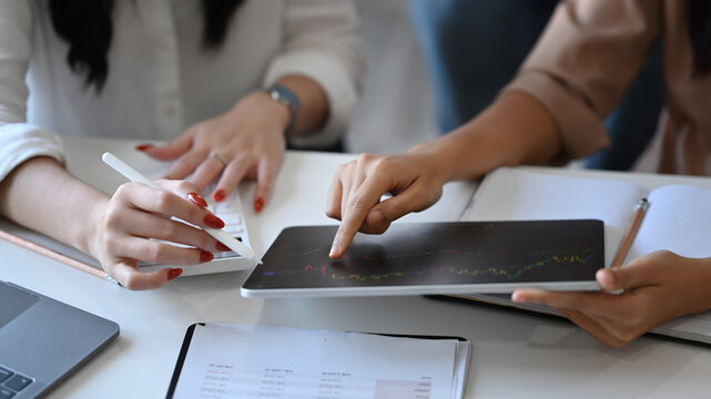 Cropped image of two business women analyzing financial graph on digital tablet together.