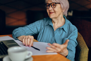 Fototapeta premium Happy senior woman sitting in a cafe with a cup of coffee and a laptop Retired woman chatting unaltered