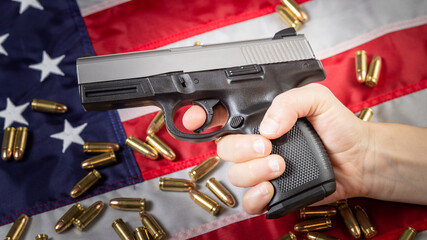 Hand holds gun against American flag. Hand gun and bullets, concept of USA firearms tradition,...