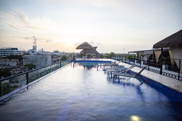 Fototapeta premium Astonishing view of pool and beach beds on rooftop with sunset as background