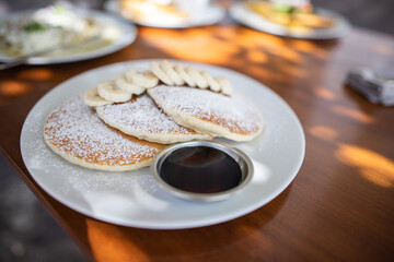 Tasty pancakes with powdered sugar and sliced banana on wooden table