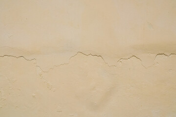 Cream colored walls. Cracked wall. Damaged surface. Straight crack in the middle. Wall paint is starting to break. Cream background. Old house cement.