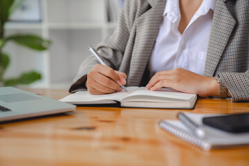 Close up of businesswomen writting notebook and working online via laptop computer for analytic business report on the workplace, freelance work from home, Planning financial and business concept.