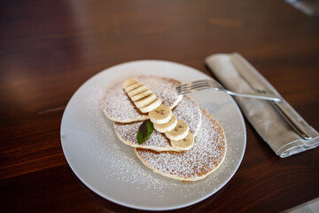 Tasty pancakes with powdered sugar and sliced banana above borwn table