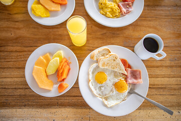 Delicious fried eggs, fruit, orange juice, and a cup of coffee on wooden table
