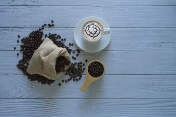 Latte art coffee in a coffee cup and coffee beans isolated with sack bag and coffee scoop on left side white wooden background