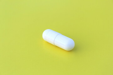 The drug in a white capsule lies alone on an isolated yellow background.