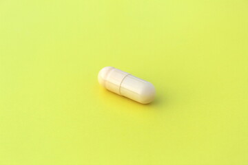 The drug in a beige capsule lies alone on an isolated yellow background.
