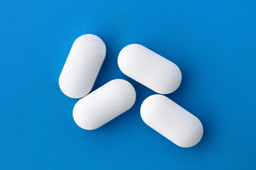 Four white oblong tablets lie on a blue background.