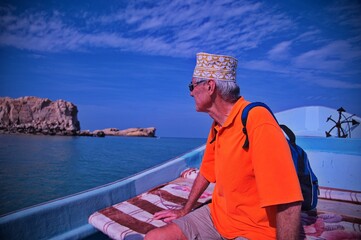Fototapeta premium Senior tourist with Oman hat sitting on the boat and sailing along the coast