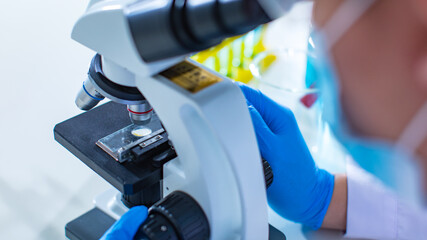 Closeup shot of microbiology defective sample on glass plate placing under microscope zooming lens while scientist hands wearing protective safety rubber gloves adjusting camera focus in laboratory